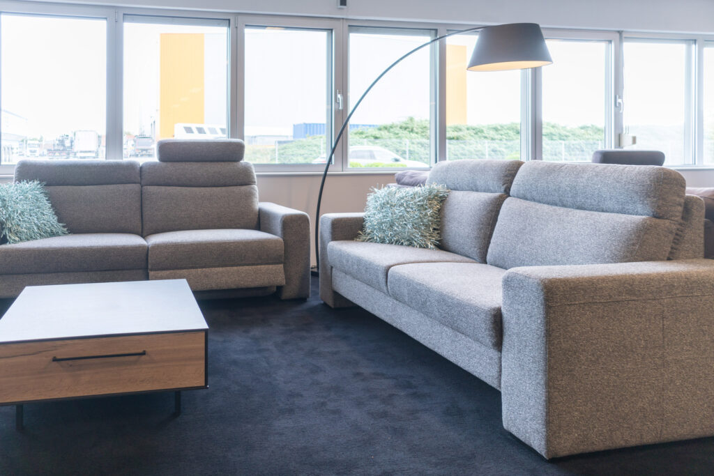 Zwei graue Stoffsofas mit Bogenlampe und Couchtisch vor der Fensterfront des Showrooms