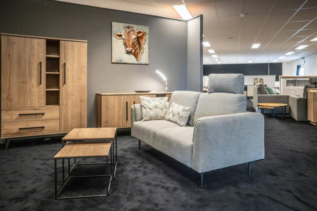 Graues Stoffsofa mit Zierkissen, Beistelltischen und Eichenschrank im Showroom