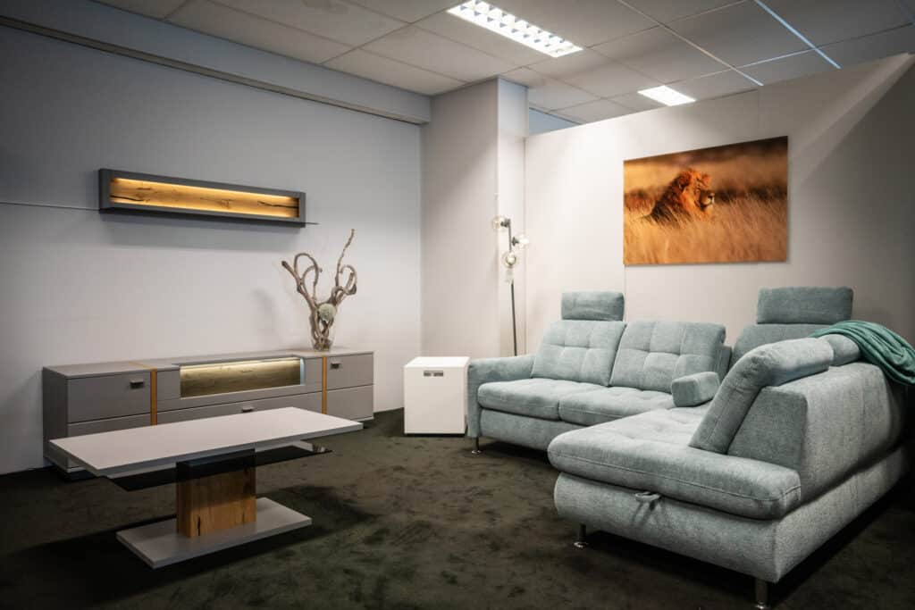 Wohnzimmer mit hellblauem Stoffsofa mit Récamiere, Couchtisch und beleuchtetem Lowboard